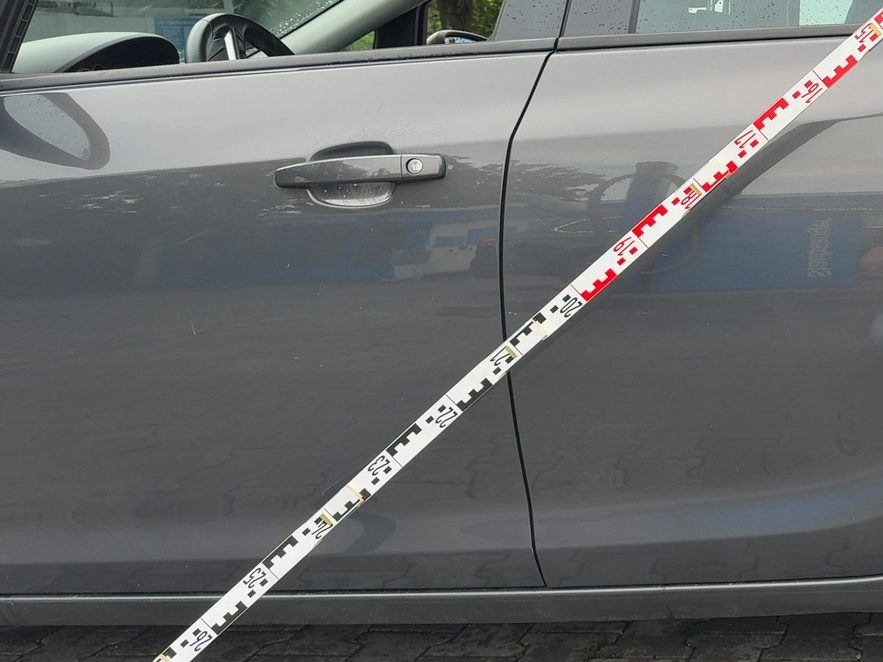 Angelegte Messlatte an der eingedrückten Fahrzeugseite während der Schadenaufnahme